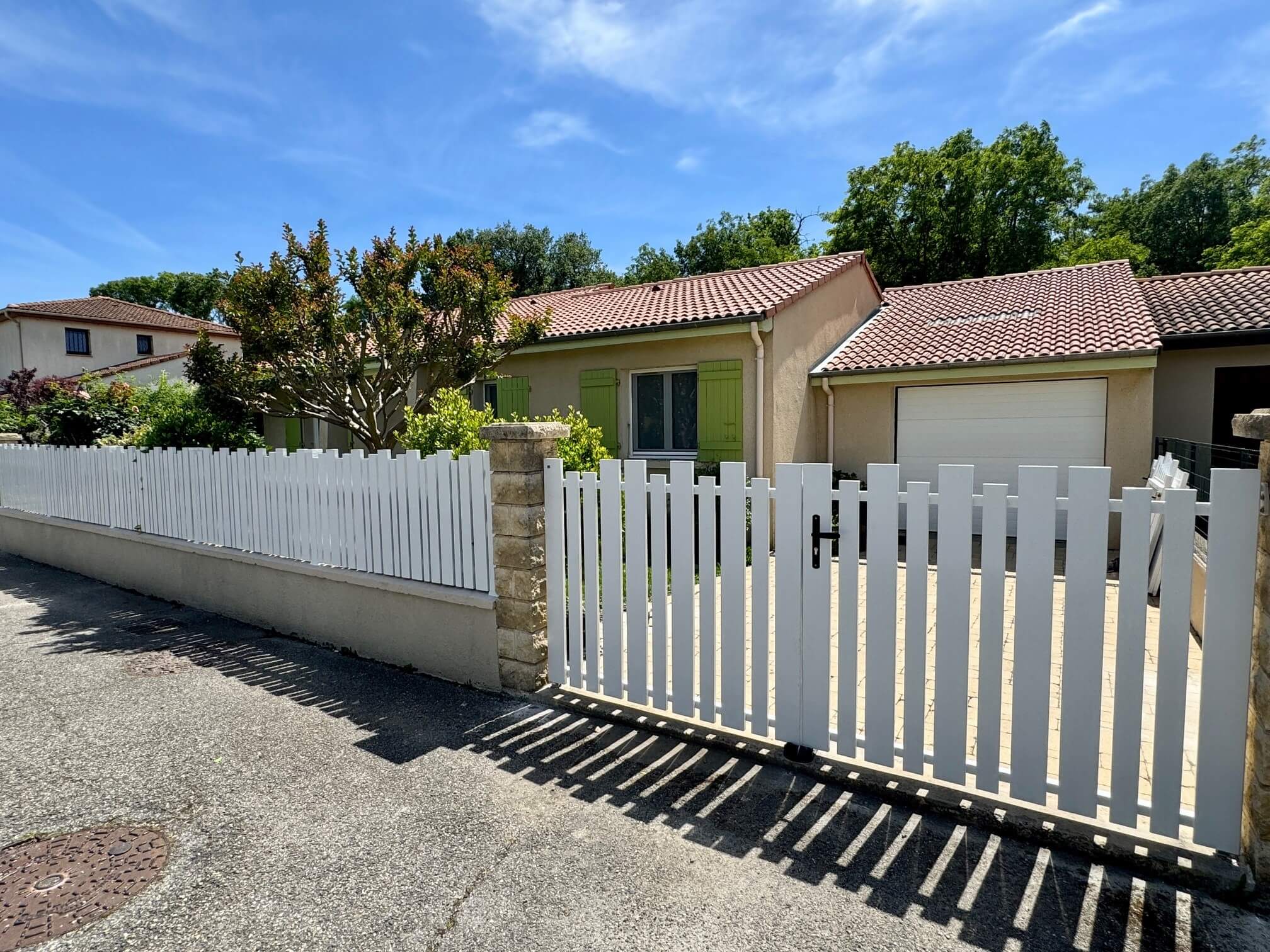 Clôture en pvc blanc ajourée installée avec une variation subtile des largeurs de lames avec portail et portillon assortis